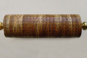 A cylinder made of several wooden disks stacked side by side lies on its side displaying the phrase 'cooljeffersoncipher' across the middle row among rows of random letters.