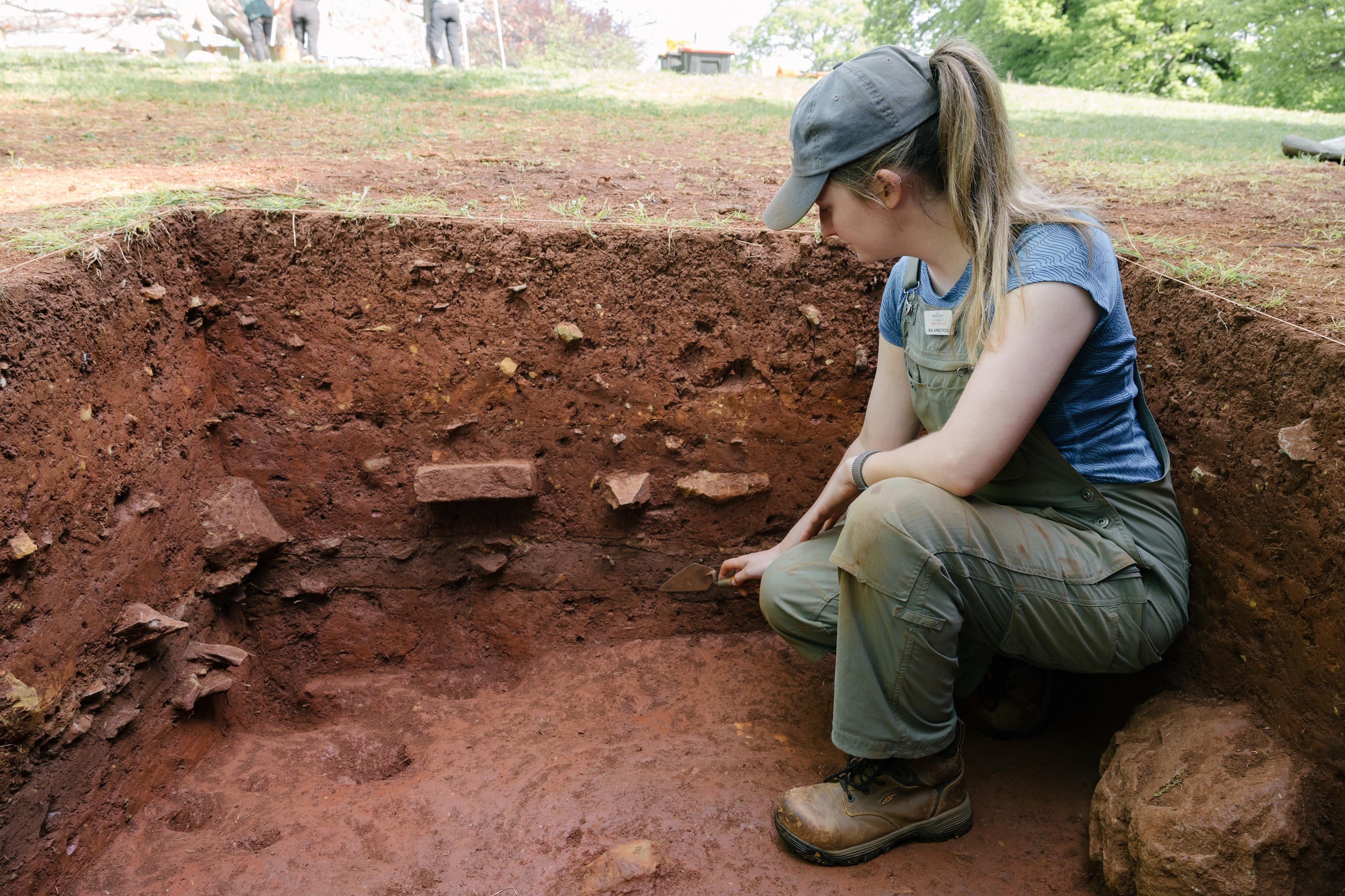 A Monticello archaeologists points to different layers in an excavation unit on the East Lawn