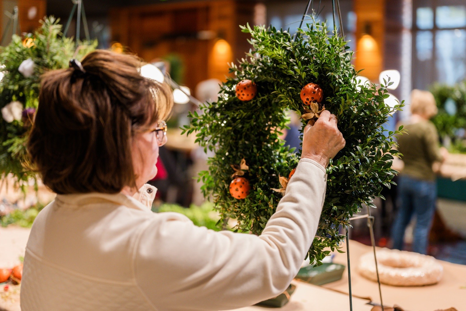 Woman decorates a Christmas wreath made of natural greenery, fruits, and dried flowers
