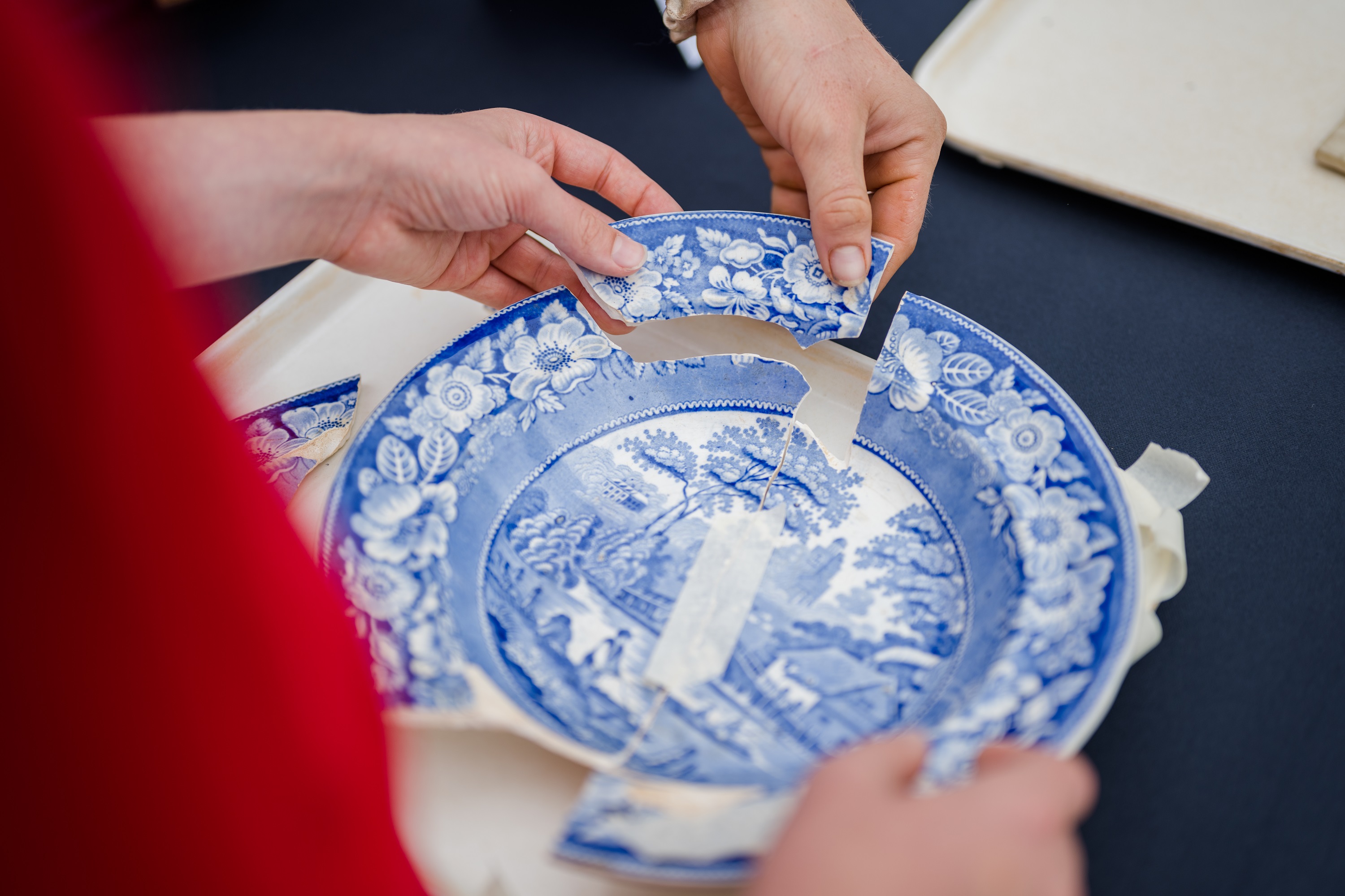 Person piecing back together broken pottery with blue decoration