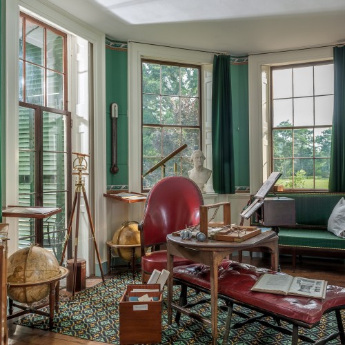 Jefferson's Cabinet office with large windows, scientific instruments, and red chair behind a crowded desk.