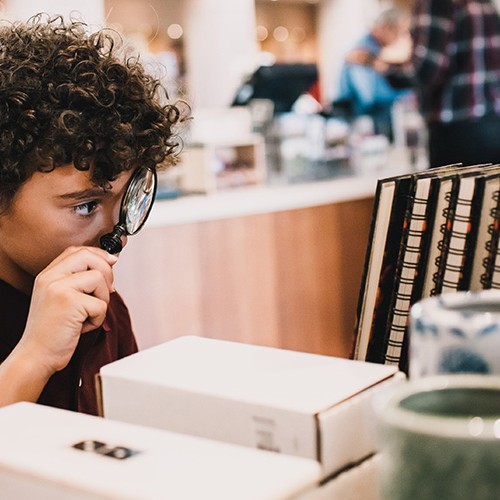 A boy using a magnifying glass looks at products in The Shop at Monticello
