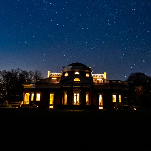 View of Monticello's west facade, including portico and dome, at night with the house lit from within and stars bright in the sky