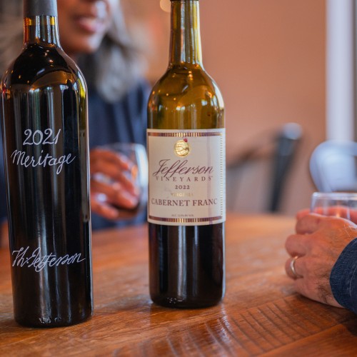Wooden table with two bottles of Jefferson Vineyards wine and two people enjyoing award-winning wine