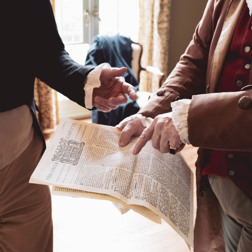 Costumed interpreters point at a colonial newspaper to promote the Founding Friends, Founding Foes Tour