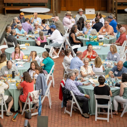Several tables of people sitting outdoors, eating and playing Feast of Reason