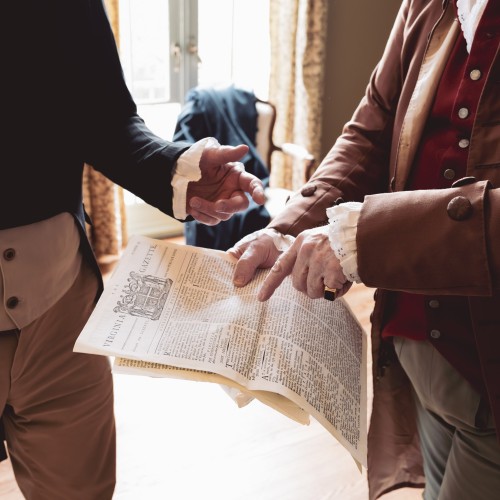 Two men in late 18th-century clothing gesture to each other over a newspaper