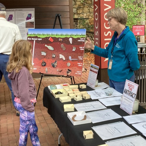 Archaeologists explain artifact and excavation displays to a young girl at an Archaeology Open House