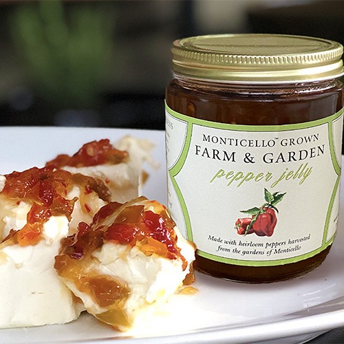 A jar of Monticello Farm & Garden Pepper Jelly sits next to jelly-topped biscuits