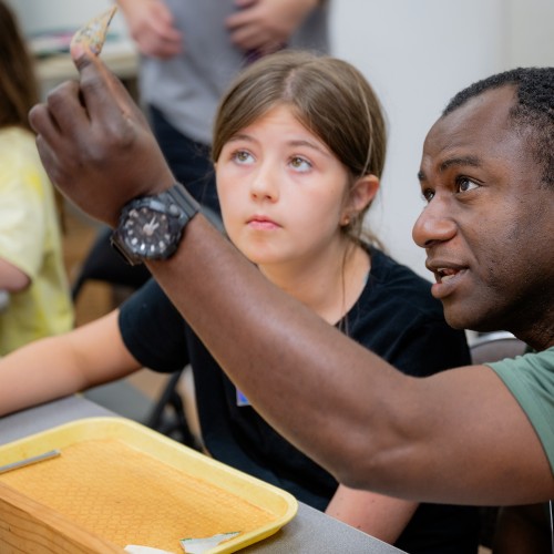 An archaeologist inspects and discusses a glass artifact with a young girl
