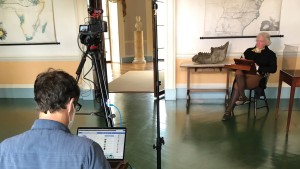 A person operates a camera and computer while an actor dressed at Thomas Jefferson sits in a chair