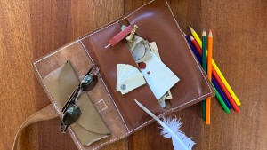 An old-fashioned notebook styled after Thomas Jefferson's note taking method, spectacles, colored pencils, and a quill rest on a table.